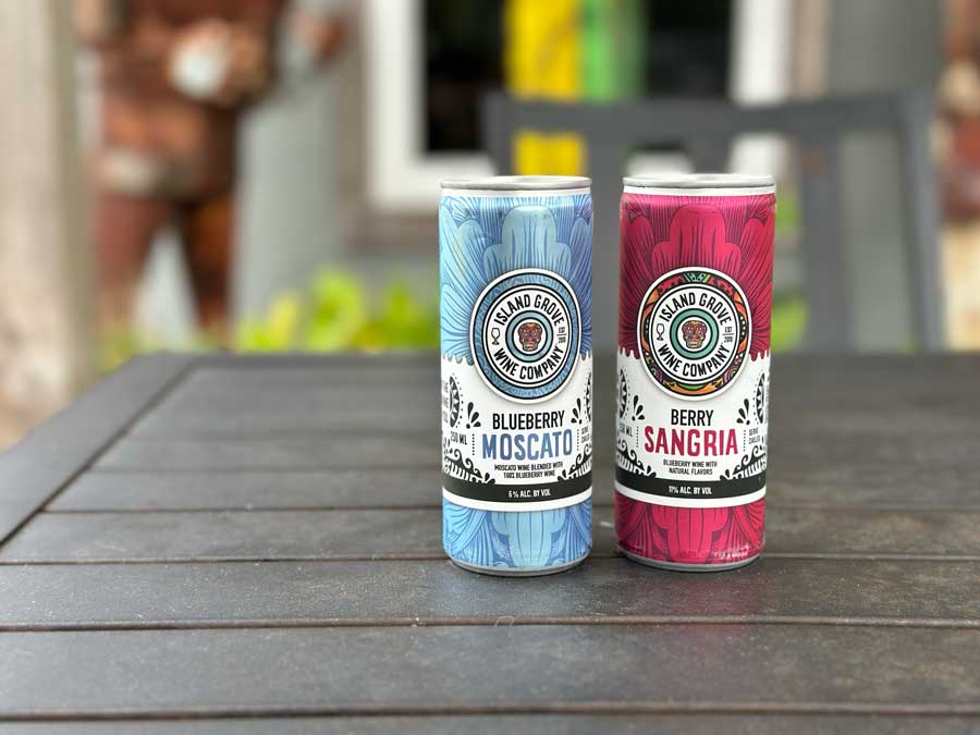 Two colorful canned wines from Island Grove Wine Company sit on an outdoor patio table, showcasing portable alternatives to hard seltzers for beach days, backyard gatherings, and refreshing ready-to-drink summer beverages.